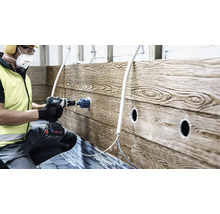 En hantverkare borrar ett hål i en väggpanel med trälook med hjälp av en sladdlös borrskruvdragare och en hålsåg.