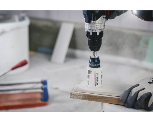 Bosch sladdlös borrskruvdragare med diamanthålsåg som borrar ett hål i en vit keramikplatta.
