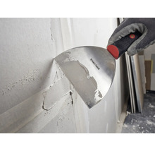 Hand i arbetshandske applicerar spackel på en vägg med en Rautner spackelspade.