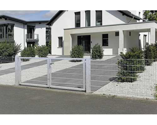 Dubbelgrind av panelstängsel och matchande staket framför ett modernt bostadshus med grusträdgård och buskar.