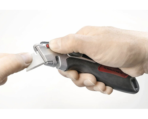 Hand som håller en Rautner trapetskniv med ergonomiskt grepp under ett bladbyte.