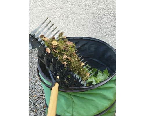 Trädgårdsräfsa med samlade löv ovanför en trädgårdssäck