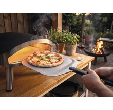 En nybakad pizza tas ut ur en bärbar pizzaugn på ett träbord i trädgården med en pizzaspade med Tenneker Logo.