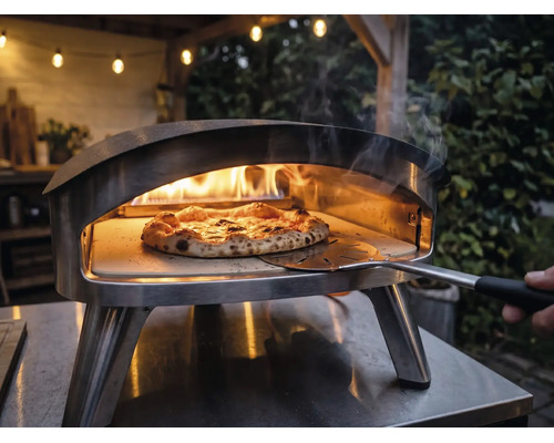 Pizzaugn i rostfritt stål för utomhusbruk med brinnande lågor och en pizza på en pizzasten som flyttas med en pizzaspade.