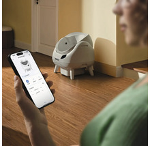 En person styr en självrengörande Catlink kattlåda via en app på en smartphone i ett ljust rum.
