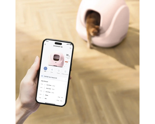 Smartphone-applikation för styrning av en självrengörande kattlåda, i bakgrunden syns enheten med en katt på ett trägolv.