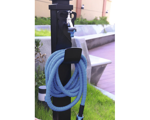 Svart vattenpost för trädgård med silverfärgad kran och en ihoprullad blå trädgårdsslang på en hållare utomhus.
