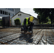 En byggarbetare i skyddsutrustning kapar armeringsnät med en Metabo batteridriven vinkelslip på en byggarbetsplats.