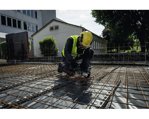 En byggarbetare i skyddsutrustning kapar armeringsnät med en Metabo batteridriven vinkelslip på en byggarbetsplats.