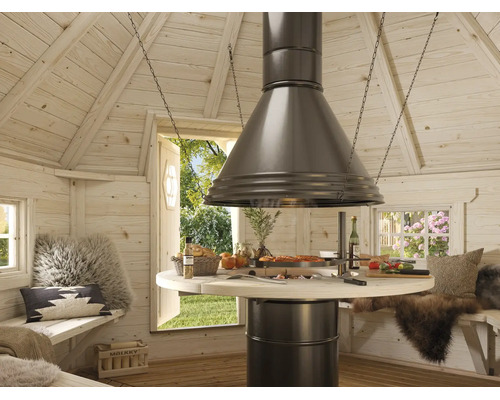 Ljus interiör av en grillkåta i trä med ett centralt runt grillbord, en stor fläktkåpa i metall och sittbänkar med kuddar.