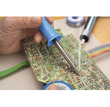 En hand löder fast en elektronisk komponent på ett grönt kretskort med en lödpenna.