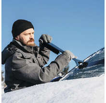 En man tar bort snö från en bilruta med en isskrapa med borste.