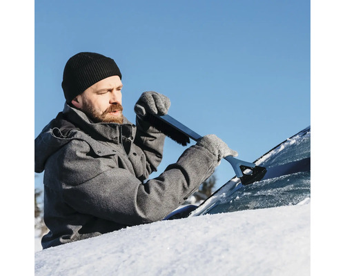 En man tar bort snö från en bilruta med en isskrapa med borste.