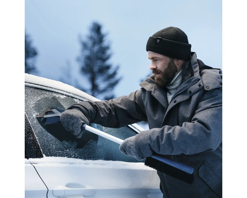 En man i vinterkläder tar bort snö från en bilruta med en isskrapa.