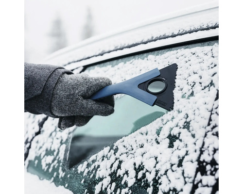 Isskrapa i handen på en person med handskar som tar bort snö och is från en bilruta