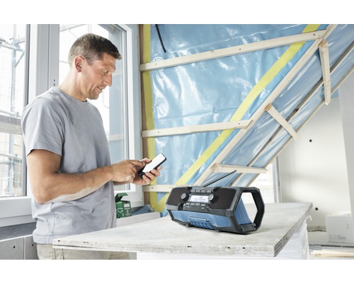 Man använder en mobiltelefon bredvid en byggplatsradio i ett rum med oavslutade väggar