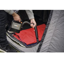 En person använder en sladdlös WORX dammsugare i ett tält.