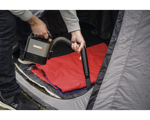 En person använder en sladdlös WORX dammsugare i ett tält.