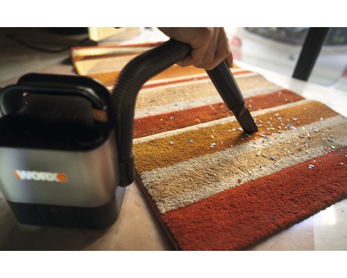 En sladdlös dammsugare används på en randig matta för att ta bort små partiklar. Worx företagslogotyp.