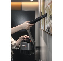 En person rengör en tavla på väggen med en bärbar Worx dammsugare.