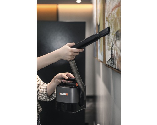 En person rengör en tavla på väggen med en bärbar Worx dammsugare.
