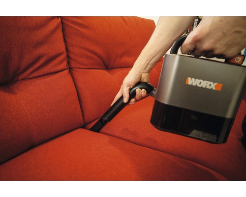Person dammsuger en soffa med en sladdlös dammsugare från Worx
