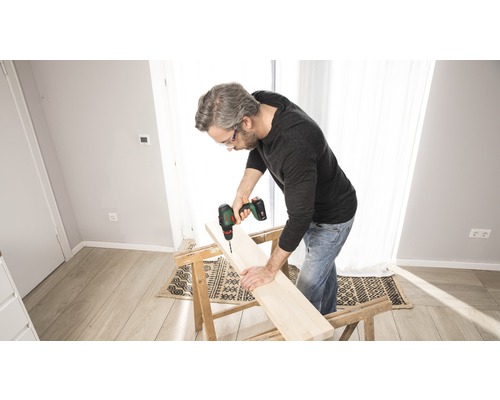 Man borrar ett hål i en träplanka med en sladdlös borr som ligger på en arbetsbänk.