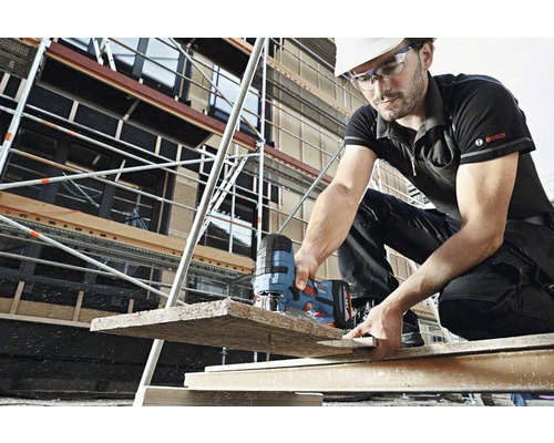 Hantverkare med skyddsglasögon och hjälm sågar en träplanka med en sticksåg framför en byggnadsställning. Bosch-logotyp.