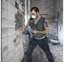 Man med andningsmask och skyddsglasögon arbetar med en borrhammare på en vägg