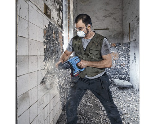 Man med andningsmask och skyddsglasögon arbetar med en borrhammare på en vägg