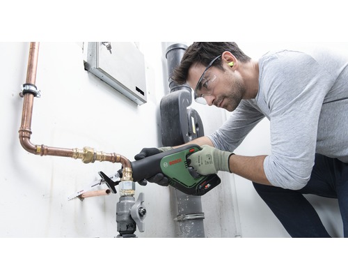 En hantverkare använder en tigersåg från Bosch för att kapa ett kopparrör. Han bär skyddsutrustning som skyddsglasögon och handskar.