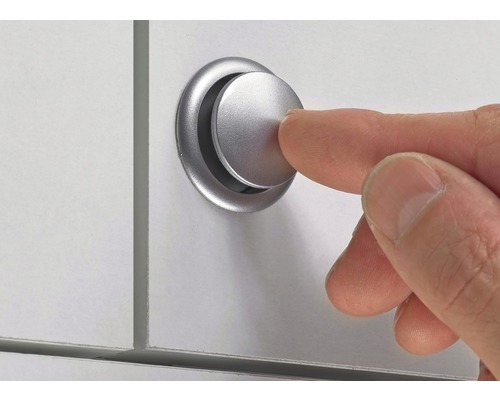 Ett finger trycker på en silverfärgad möbelknapp på en vit yta