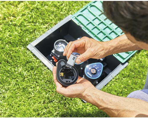 Man sätter i batteri i bevattningsdator i en brunn i gräsmattan