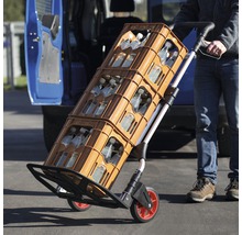 En säckkärra transporterar dryckeslådor framför ett fordon.