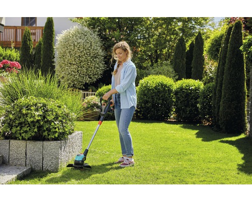 Kvinna klipper gräs med en grästrimmer i trädgården.