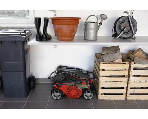 Scen med soptunna, gummistövlar, blomkruka, vattenkanna, kabelvinda, gräsklippare och trälådor i förrådet