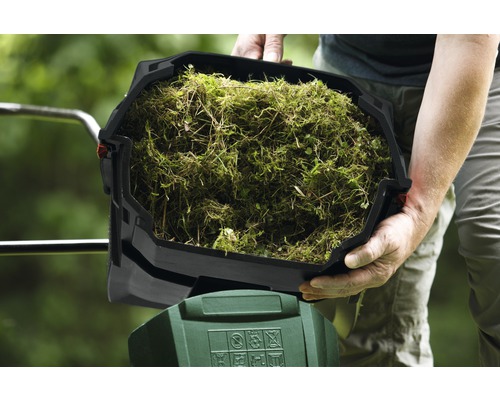 Person håller en behållare med gräsklipp ovanför ett trädgårdsredskap