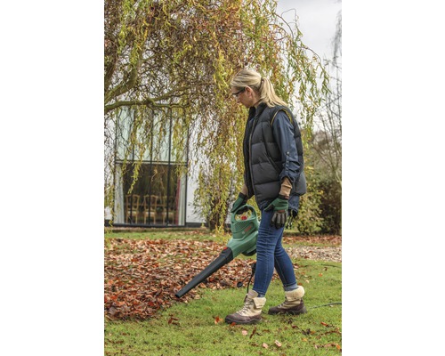 Kvinna använder en lövsug i trädgården för att ta bort höstlöv.