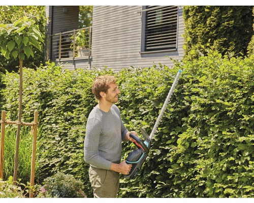 Man klipper häck med en häcksax i trädgården.