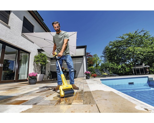 Man rengör stenterass med en borste för terrassrengöring nära en pool.