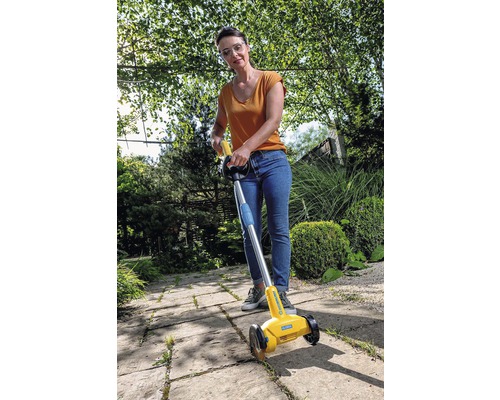 Kvinna använder en fogskrapa för att ta bort ogräs på en trottoar.