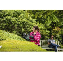 Kvinna klipper häck med häcksax i trädgården.