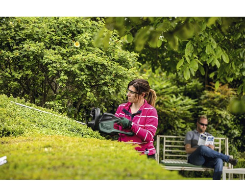 Kvinna klipper häck med häcksax i trädgården.