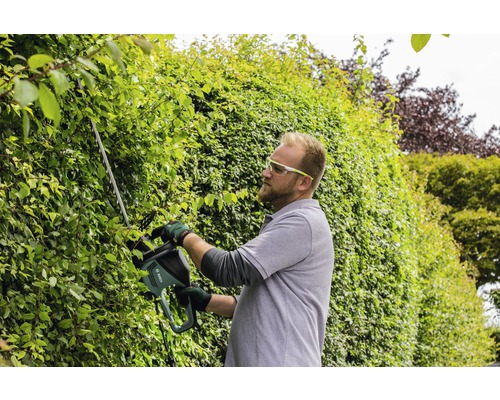 Man klipper häck med häcksax i trädgården