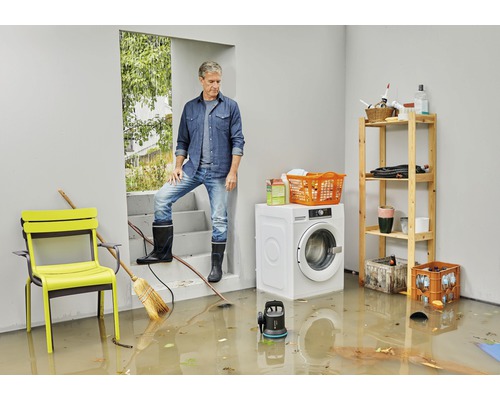 Översvämmad källare med man, tvättmaskin, möbler och dränkbar pump