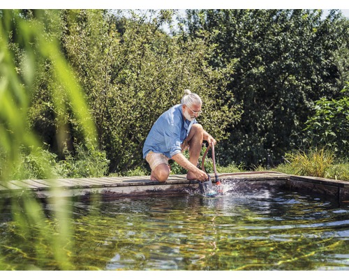 En man knäböjer vid dammkanten och rengör dammen med en dammsugare.