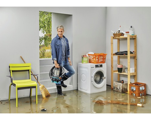 Man med dränkbar pump i översvämmad källare med tvättmaskin och hylla