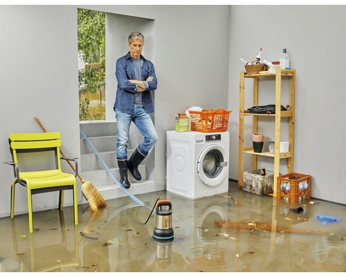 Översvämmad källare med stående vatten, dränkbar pump, tvättmaskin, hylla och man