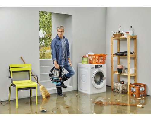 Man med dränkbar pump i översvämmad källare med tvättmaskin och hylla