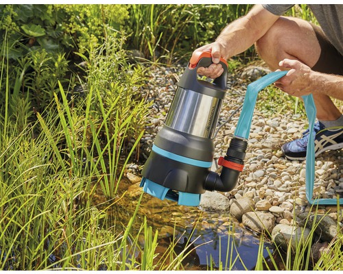 En person håller en Gardena dränkbar smutsvattenpump med ansluten slang över en damm